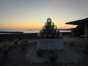 日本の夕陽百選の三重県志摩市浜島町の目戸山海岸前のビン球ロード 絆の灯モニュメントと夕日
